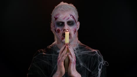 Frightening-man-with-Halloween-zombie-bloody-makeup-spells-conjures-over-candle,-voodoo-rituals
