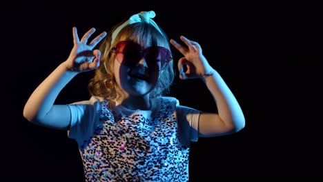 Portrait-of-young-blond-girl-in-bright-colorful-neon-rays-light-showing-ok-sign-on-black-background