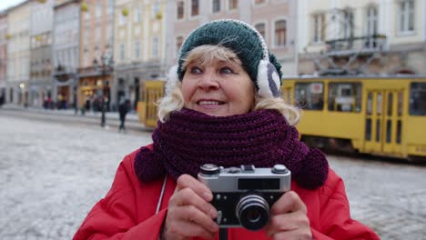 Senior-old-woman-tourist-taking-pictures-with-photo-camera,-using-retro-device-in-winter-city-center