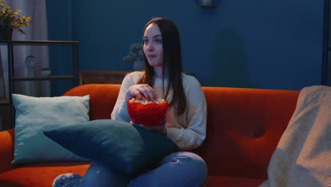 Frau-Sitzt-Allein-Auf-Dem-Sofa,-Isst-Popcorn-Und-Sieht-Sich-Zu-Hause-Eine-Interessante-Fernsehserie-Oder-Einen-Horrorfilm-An