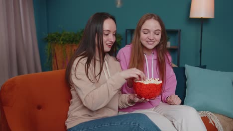 Chicas-Emocionadas,-Amigas,-Hermanos,-Divirtiéndose-Viendo-El-Partido-Deportivo-Favorito-De-La-Televisión,-Comiendo-Palomitas-De-Maíz,-En-El-Sofá-De-Casa