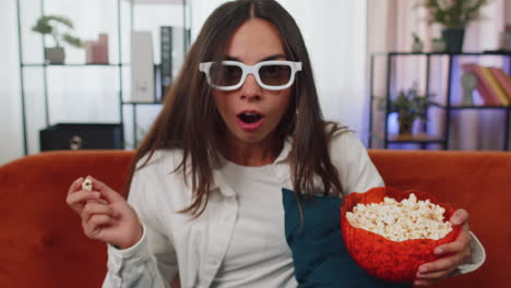 Mujer-Sentada-En-El-Sofá-Comiendo-Palomitas-De-Maíz-Y-Viendo-Interesantes-Series-De-Televisión,-Juegos-Deportivos-En-Línea-En-Casa