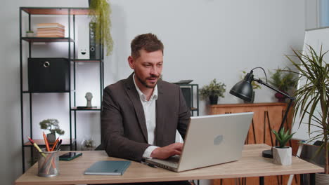 Businessman-working-on-laptop-smiling-friendly-at-camera-and-waving-hands-gesturing-hello-at-office