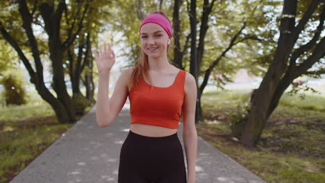 Chica-Corredora-De-Fitness-Atlético-Saludando-Con-La-Palma-De-Su-Mano-Saludando-Con-Una-Sonrisa-Hospitalaria-Y-Amistosa