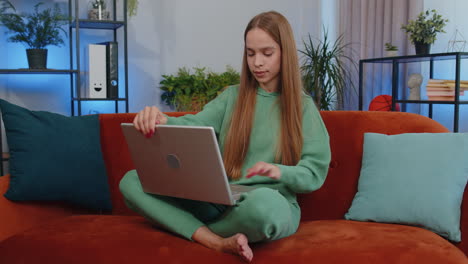 Young-teen-girl-freelancer-starts-working-on-laptop,-sends-messages,-makes-online-purchases-at-home