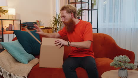 Happy-young-man-shopper-unpacking-cardboard-box-delivery-parcel-online-shopping-purchase-at-home