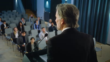 Minister,-politician-or-activist-delivers-speech-from-the-stage,-gives-interview-for-media.-Journalists-sit,-listen-and-writes-down-the-answers-during-press-campaign-in-the-conference-room.-Back-view.