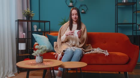 Portrait-of-smiling-young-adult-woman-in-warm-white-sweater-drink-hot-beverage-mug-relaxing-at-home