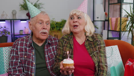 Happy-senior-family-man-woman-celebrating-birthday-anniversary-hold-cupcake-makes-wish-at-home