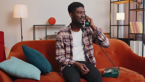 Young-adult-african-american-man-enjoying-talking-on-retro-phone-conversation-with-friends-at-home