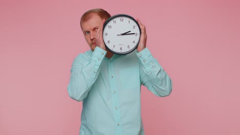 Young-man-holding-clock-watch,-hiding,-checking-time-on-clock,-running-late-to-work-being-in-delay