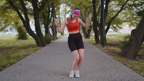 Sport-runner-pretty-girl-training-exercise-listening-music-on-headphones-dancing-having-fun-in-park