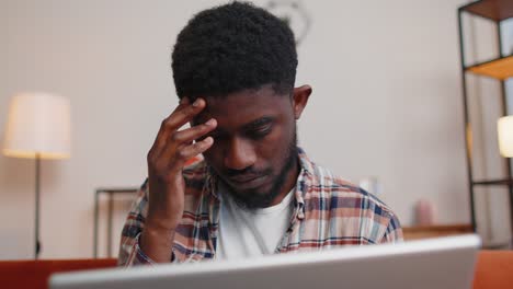 African-American-man-sitting-on-sofa-opening-laptop-pc-starting-work-online-in-living-room-at-home