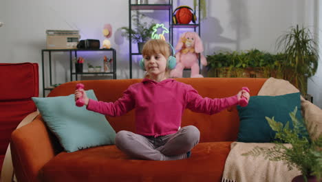 Child-kid-girl-lifting-dumbbells-while-doing-exercises,-enjoying-training,-listening-music-at-home