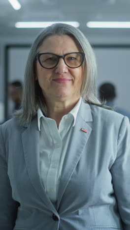 Portrait-of-mature-woman,-United-States-of-America-elections-voter.-Businesswoman-stands-in-a-modern-polling-station,-poses-and-looks-at-camera.-Background-with-voting-booths.-Concept-of-civic-duty.