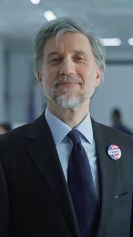 Portrait-of-businessman,-United-States-of-America-elections-voter.-Mature-man-stands-in-a-modern-polling-station,-poses-and-looks-at-camera,-smiles.-Background-with-voting-booths.-Civic-duty-concept.