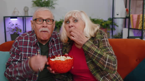 Pareja-De-Ancianos-Abuelos-Hombre-Mujer-Viendo-Una-Interesante-Película-De-Fútbol-En-Televisión,-Comiendo-Palomitas-De-Maíz