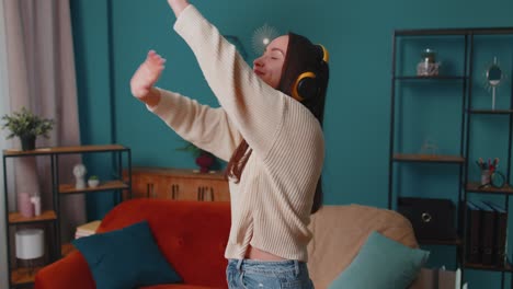 Overjoyed-young-woman-in-wireless-headphones-dancing,-singing-on-cozy-couch-in-living-room-at-home