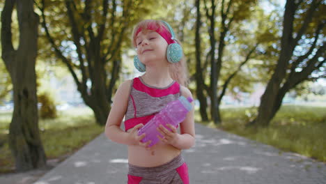 Fitness-sport-runner-child-girl-in-headphones-listening-favorite-music-song-holding-water-bottle