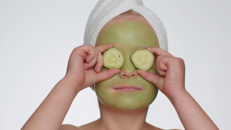 Beautiful-smiling-child-girl-kid-in-towel-on-head-applying-cleansing-moisturizing-green-mask-on-face