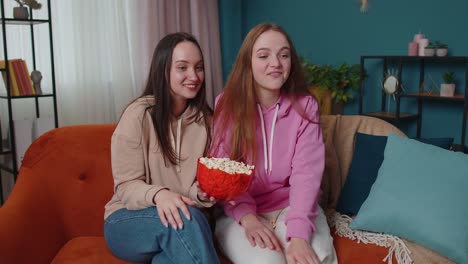 Dos-Amigas-Hermanas-Viendo-La-Película-Favorita-De-Su-Programa-De-Televisión,-Comiendo-Palomitas-De-Maíz,-Sentadas-En-El-Sofá-De-Casa