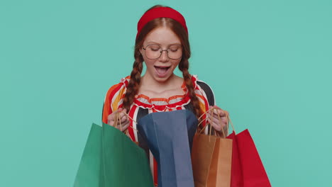 Chica-Pelirroja-Mostrando-Bolsas-De-Compras,-Descuentos-Publicitarios,-Sonriendo-Y-Sorprendida-Con-Precios-Bajos