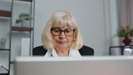 Eine-Hochrangige-Freiberufliche-Geschäftsfrau-Sitzt-Am-Arbeitsplatz-Und-Benutzt-Einen-Laptop,-Während-Sie-Im-Büro-Surft