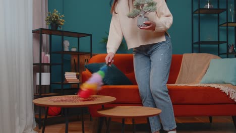 Joyful-young-woman-dusting-furniture-caring-for-hygiene-using-colorful-duster-in-living-room-at-home