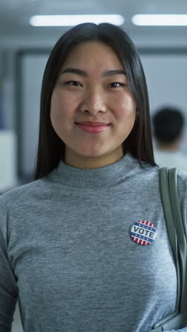 Portrait-of-mature-woman,-United-States-of-America-elections-voter.-Businesswoman-stands-in-a-modern-polling-station,-poses-and-looks-at-camera.-Background-with-voting-booths.-Concept-of-civic-duty.