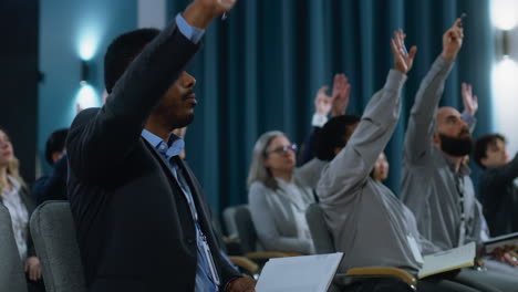 Journalists-sit-and-write-answers-in-notebooks-from-politician-during-press-campaign-in-the-conference-hall.-Caucasian-male-media-representative-raises-his-hand-and-asks-questions-during-interview.