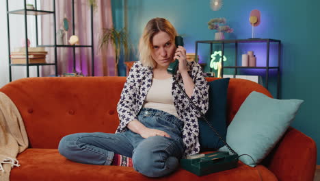 Smiling-young-woman-making-wired-telephone-call-conversation-with-friends-sitting-on-home-couch