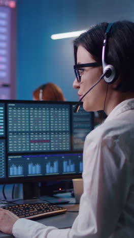 Female-financial-analyst-and-investment-manager-discuss-real-time-stocks-data-on-computer.-Colleagues-work-in-bank-office.-Big-digital-screens-showing-exchange-market-charts.-Vertical-shot