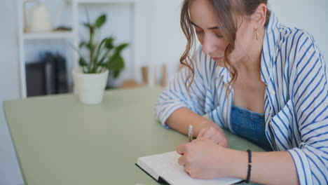 Frau-Macht-Sich-Notizen-Im-Notizbuch,-Während-Sie-Zu-Hause-Am-Schreibtisch-Lernt