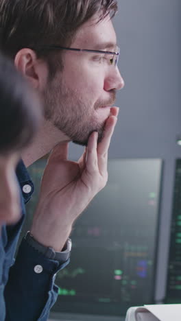 Financial-analysts-work-on-multi-monitor-computer-with-real-time-stocks-and-exchange-market-charts-in-bank-office.-Big-digital-screen-showing-TV-news-broadcast.-Vertical-shot