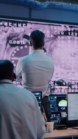 Pan-right-view-of-team-of-anonymous-operators-watching-spacecraft-docking-to-orbital-station-on-large-screen-in-mission-control-center