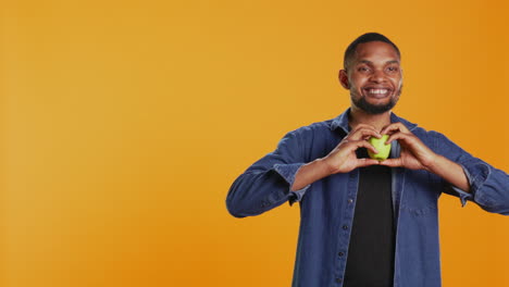 African-american-relaxed-guy-does-a-heart-shape-sign-with-an-apple