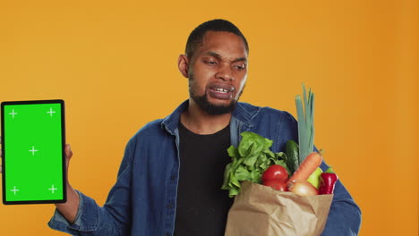 Vegan-adult-holding-a-tablet-with-greenscreen-layout-in-studio