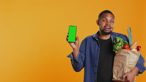 Junger-Erwachsener-Hält-Ein-Smartphone-Mit-Greenscreen-Layout-Im-Studio