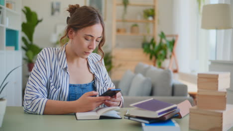 Studentin-Surft-Mit-Ihrem-Smartphone,-Während-Sie-Am-Schreibtisch-Lernt