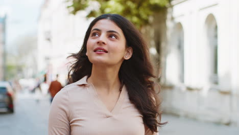 Portrait-of-Indian-woman-tourist-walking-in-urban-city-street,-smiling-having-positive-good-mood