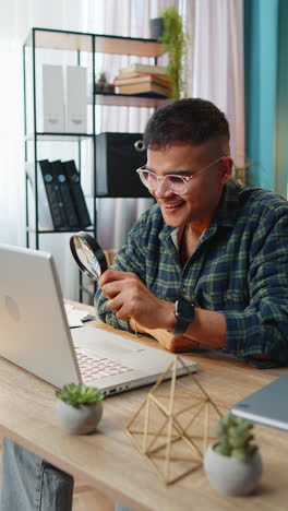 Business-man-working-at-home-office-holding-magnifying-glass-looking-at-laptop-screen-wow-expression