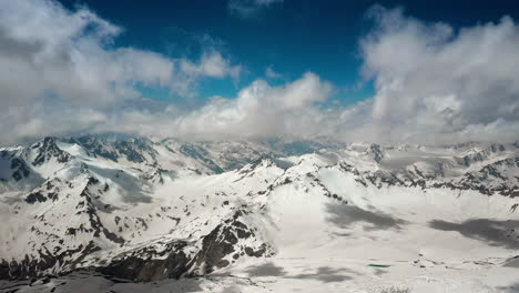 Air-flight-through-mountain-clouds-over-beautiful-snow-capped-peaks-of-mountains-and-glaciers.