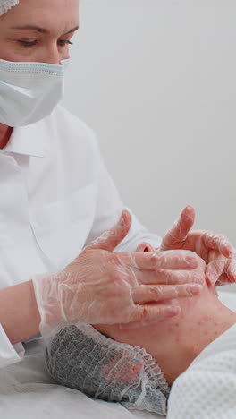 Esteticista-Aplicando-Una-Mascarilla-Hidratante-Relajante-En-La-Cara-De-Una-Mujer-Adulta-Joven-Para-Rehidratar-La-Piel-De-La-Cara