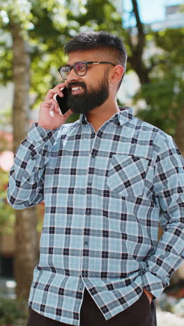Happy-Indian-man-having-remote-conversation-talking-on-smartphone,-good-news-gossip-in-city-street