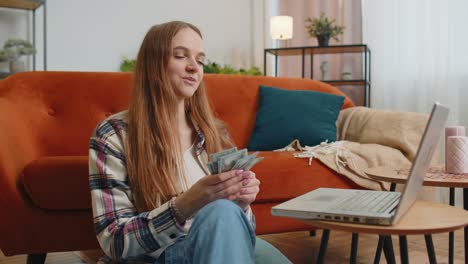 Smiling-happy-young-woman-counting-money-cash-and-use-laptop-pc-calculate-domestic-bills-at-home