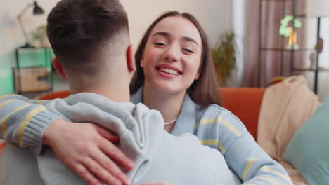 Portrait-of-woman-embracing,-hugging-man,-looking-at-camera-over-his-shoulder-at-home-room,-support