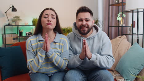 Young-family-marriage-couple-praying-sincerely-with-folded-arms-asking-God-for-help,-begging-apology