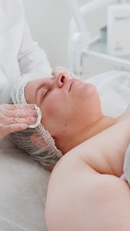 Cosmetologist-doctor-wipes-woman-face-and-neck-cleaning-procedure-with-cotton-pads-in-beauty-clinic