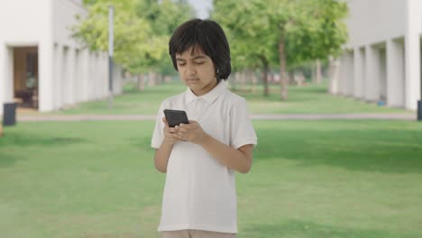 Niño-Indio-Enojado-Enviando-Mensajes-De-Texto-A-Alguien-Por-Teléfono-En-El-Parque