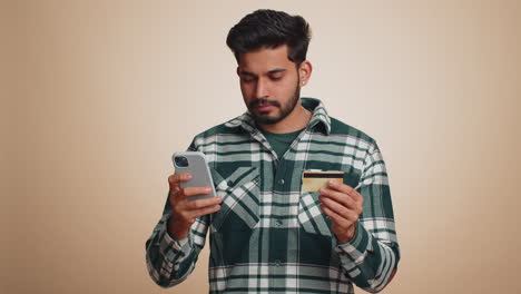 Indian-man-using-credit-bank-card-and-smartphone-while-transferring-money-purchases-online-shopping